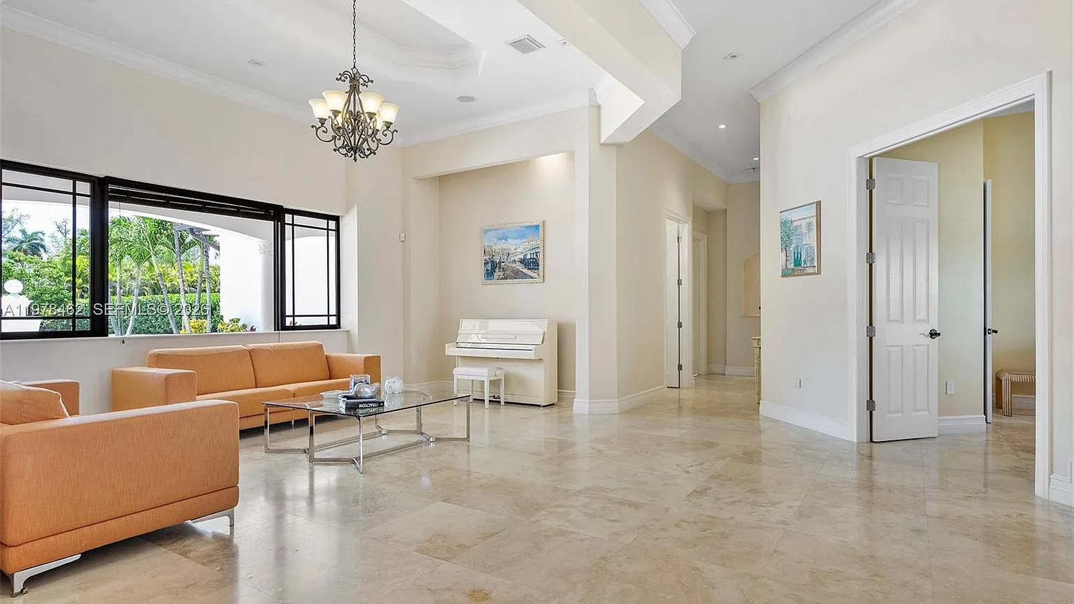 Real MLS listing photo: the formal living room with orange sofas, a white piano, chandelier and travertine floors