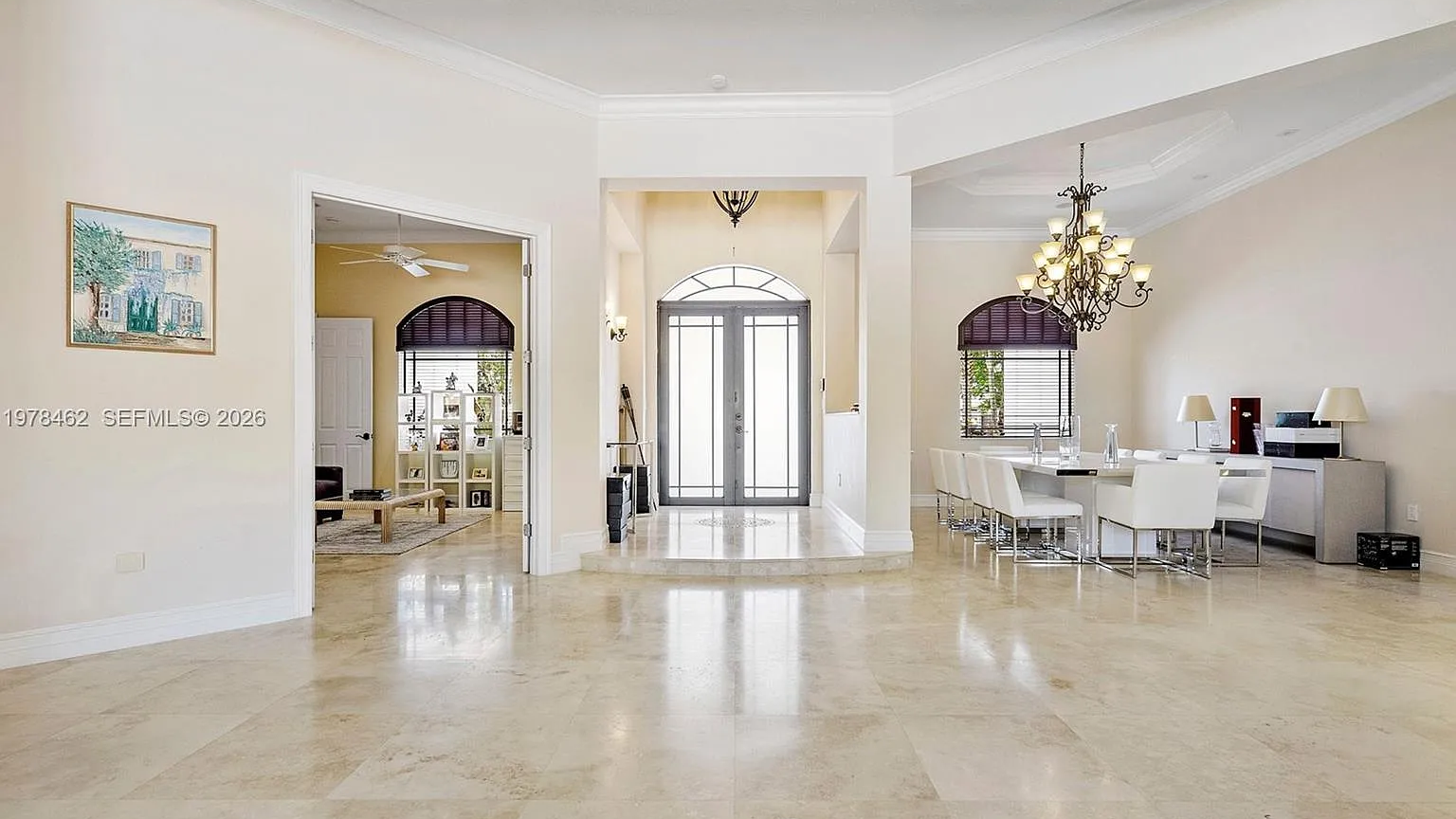 Real MLS listing photo: the foyer with arched double entry doors, a chandelier and the white dining table