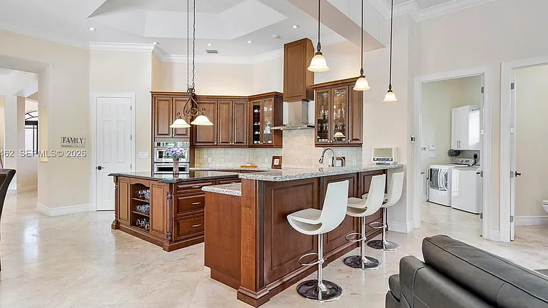 Real MLS listing photo: the kitchen with wood cabinetry, granite island, pendant lights and white bar stools